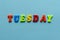Word `tuesday` of colored plastic magnetic letters on blue paper background