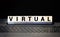 The word VIRTUAL is written on a wooden block on a computer keyboard. Internet concept