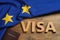 Word Visa made of wooden letters, passport and European Union flag on table, flat lay
