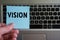 Word VISION on sticky note hold in hand on keyboard background