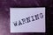 The word Warning on a white Notepad.