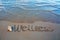 Word Wellness written on the sand near the sea.Vacation concept.