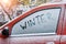 Word Winter written with finger on a snowy side window of a car