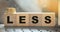 Less word on wooden cubic blocks with letters and stack of coins on it. Selective focus. Spend less or cut costs business concept