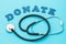 Word from wooden letters and medical stethoscope on blue background, concept on the topic of donation for treatment