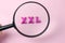 The word XXL from wooden bright letters under a magnifying glass on a light pink background