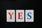 The word yes made up of letters of blue and red on white cards laid out in a line on a black background