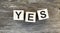 The word Yes. written in black letters on wooden blocks. Message spells Yes on white background.