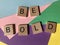 The words Be Bold isolated on a multicoloured background