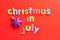 The words christmas in July in colorful letters on a red background