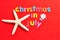 The words christmas in July in colorful letters with a starfish and a Santa figurine