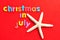 The words christmas in July on a red background with a starfish