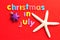 The words christmas in July on a red background with a starfish and a star shape bauble
