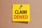 Words claim denied written on yellow square paper and pinned on craft paperboard