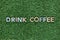 The words Drink coffee made from multicolored letters on grass background, shot from above, aligned in the center