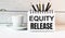 The words EQUITY RELEASE is written in a white notepad near a white cup of coffee on a light background