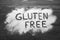 Words Gluten free written with flour on dark wooden table, top view