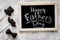 Words happy Father`s day written on blackboard. Black tie, mustache and hat cookies. Grey stone background top view