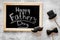 Words happy Father`s day written on blackboard. Black tie, mustache and hat cookies. Grey stone background top view