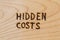 The words hidden costs handwritten with woodburner on flat wood surface - directly above flat lay composition view