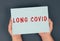 The words long covid are standing on a paper, hands hold the message, problems after covid-19