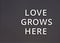 Words Love Grows Here spelled out with white letters on gray pegboard