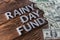 Words RAINY DAY FUND laid on wooden surface by metal letters with rain drops and us dollar banknotes