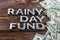 Words RAINY DAY FUND laid on wooden surface by metal letters with rain drops and us dollar banknotes