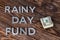 The words RAINY DAY FUND near small pack of us dollars on wooden background