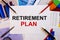 The words RETIREMENT PLAN is written on a white background near colored graphs, pens and pencils. Business concept