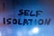 The words self isolation handwritten on wet window glass at night - close-up full frame picture with selective focus