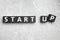 Words START UP made with black cubes on grey marble background, flat lay