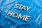 The words stay home laid with silver metal letters on crumpled blue plastic background in slanted diagonal perspective