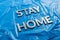 The words stay home laid with silver metal letters on crumpled blue plastic background in slanted diagonal perspective