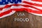 words USA proud laid with silver metal letters on brown wooden surface with flag of United States of America