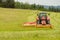 Work on an agricultural farm. A red tractor cuts a meadow.