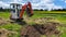 Work on the construction site of a house. The excavator digs out roots. A small digger in the garden