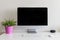 Work desk with a computer and a houseplant with a pink pot  against a white wall