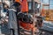 Work driller in red uniform, in helmet and goggles. He uses a hydraulic wrench to screw drill pipes to lower them into an oil well