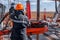 Work driller in red uniform, in helmet and goggles. He uses a hydraulic wrench to screw drill pipes to lower them into an oil well