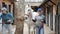 Daily work in horse yard. Smiling older female stable keeper leading white racehorse to riding arena,