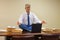 Work related stress relief with yoga as man does pose with stacks of paperwork and computer on conference table