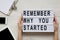 Work space with tablet, smartphone, sheet and `Remember why you started` words on lightbox on white wooden table. Female hands h