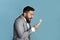 Work stress. Angry businessman shouting into landline phone receiver against blue background