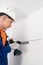 A worker attaches to the white wall the fasteners for hanging kitchen cabinets using an electric screwdriver