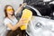 Worker beautiful woman cleaning auto black foam with yellow sponge. Car washing service