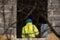 Worker with blue plastic helmet on head and yellow reflecting vest works at building yard