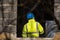 Worker with blue plastic helmet on head and yellow reflecting vest works at building yard