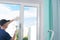 A worker in a blue uniform installs a double-glazed window in a plastic window frame, fixing it with a rubber mallet