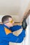 A worker in a blue uniform screws a wooden block to the concrete ceiling with a screwdriver